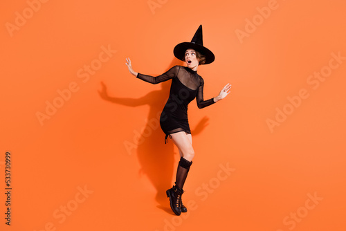 Full body photo of cute girl look frighten empty space escape dressed trendy black halloween garment isolated on orange color background