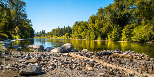 Fototapeta Naklejka Na Ścianę i Meble -  Autumn Rogue River and Riverside park forest landscape over the rocky beach with ruined pilings in Grants Pass, Oregon