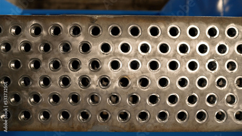 Metal part with many holes for filtering. Plant for the production of metal pipes.Pile of long drill rods metal workpieces in light warehouse. Heavy industry.