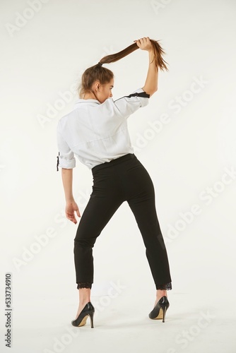A girl in a white shirt stands against a white isolated background and pulls her hair.
