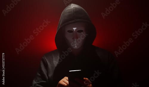 Man wearing mask with hoodie launches virus from smartphone.
