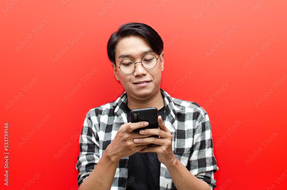 Asian man looks surprised at screen of mobile phone. happy asian man with gesture while holding phone. wow expression. asian man with glasses holding phone. Asian man looks surprised at screen of mobile phone. happy asian man with gesture while holding phone. wow expression. asian man with glasses holding phone.