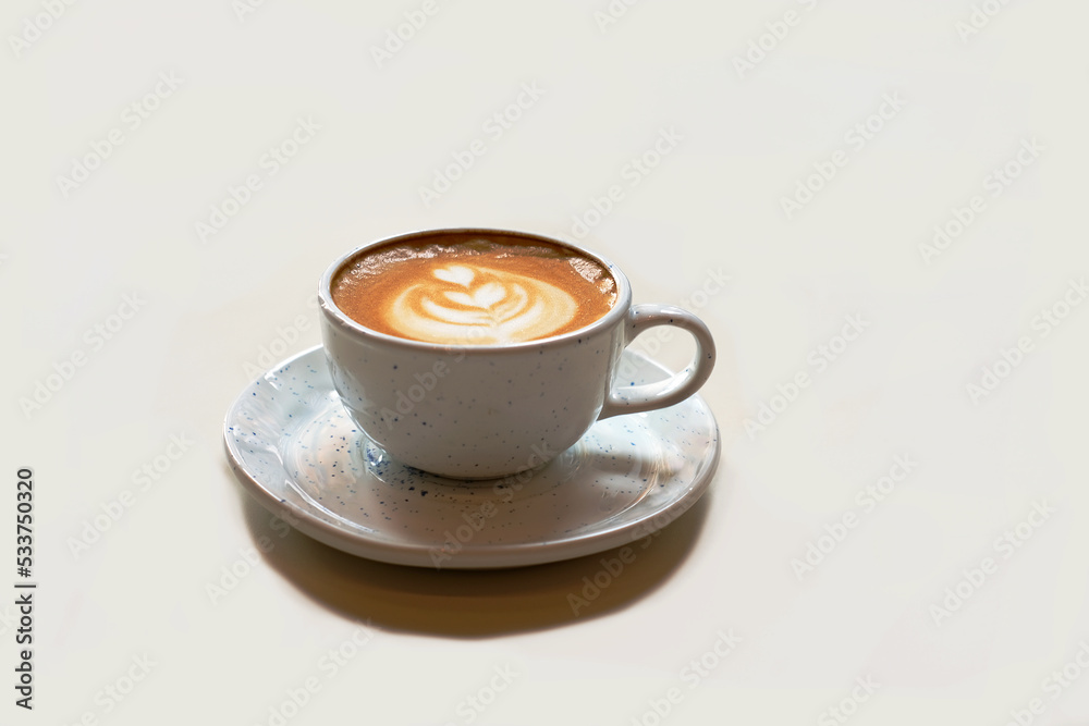 Hot coffee with latte art in ceramic white cup and saucer on light shade of platinum. Cappuccino coffee. Close-up Hot coffee with latte art in ceramic white cup and saucer on light shade of platinum. Cappuccino coffee. Close-up