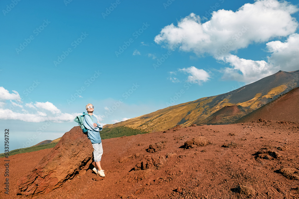 Happy tourist woman enjoying freedom, while admiring panoramic view of colorful summits of active volcano Etna, Tallest volcano in Continental Europe, Sicily, Italy.