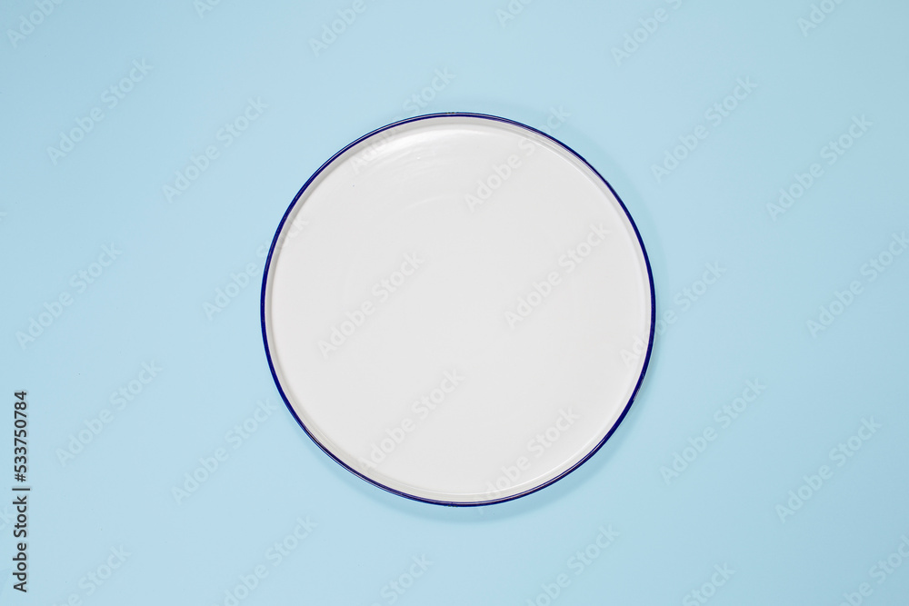 white plate in the center, top view, copy space. On a blue background - obrazy, fototapety, plakaty 