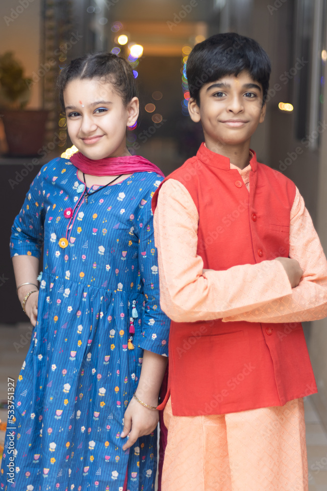 2 Indian kids, brother and sister friends siblings dressed up in ethnic wear smiling looking at the camera celebrating diwali Hindu festival Laxmi poojan with ambient light bokeh 2 Indian kids, brother and sister friends siblings dressed up in ethnic wear smiling looking at the camera celebrating diwali Hindu festival Laxmi poojan with ambient light bokeh