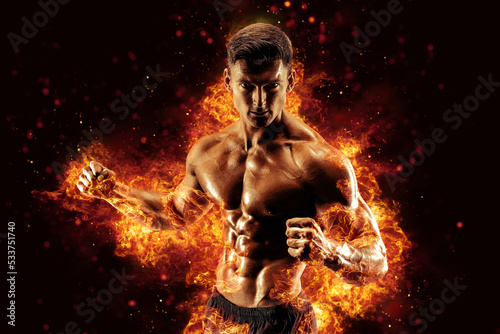 Bodybuilder posing on the fire flames background © zamuruev