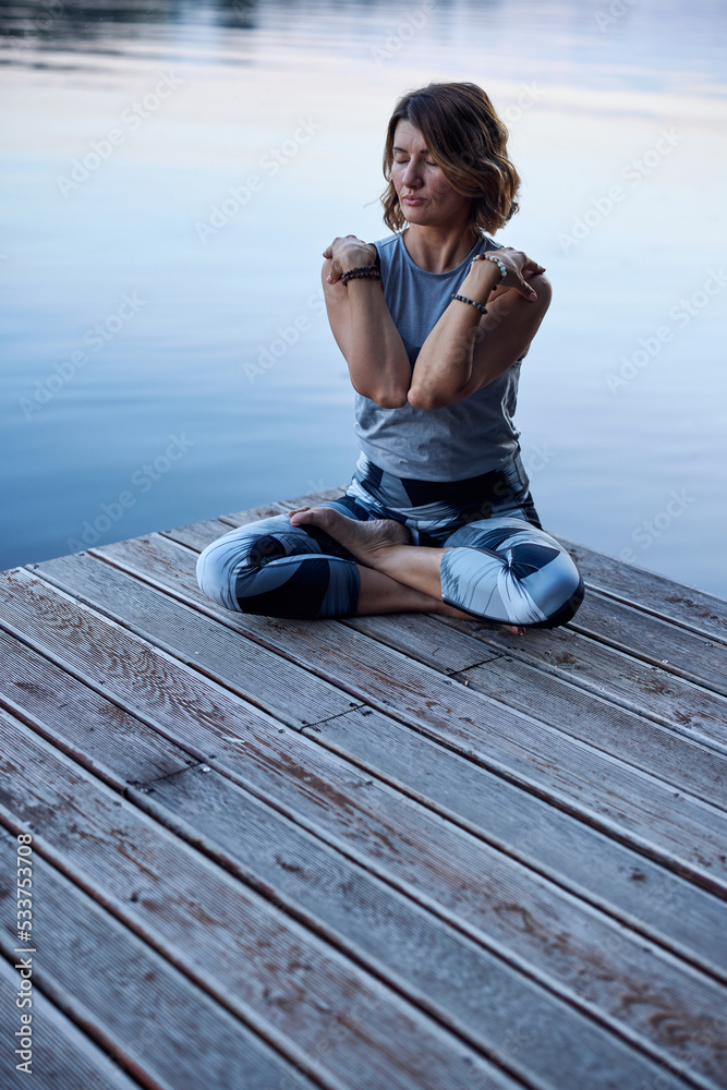 A calm woman sits in a lotus yoga pose and practices breathing exercises.