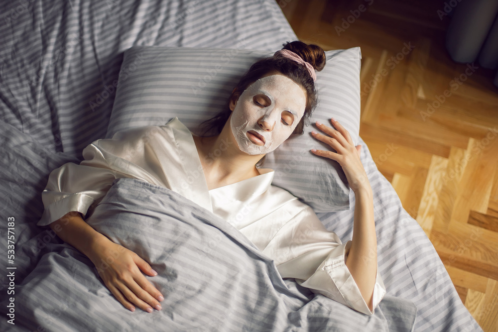 sexy brunette woman lies with her back on the bed in front of the bedroom window in a rejuvenating mask on her face. sexy brunette woman lies with her back on the bed in front of the bedroom window in a rejuvenating mask on her face.