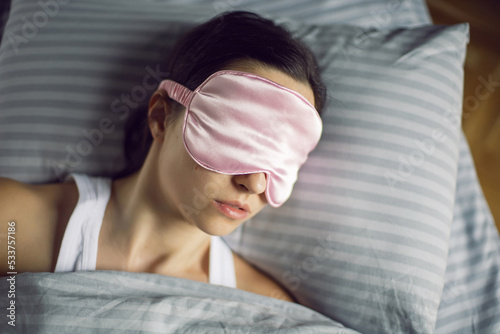 woman in a pink eye mask lies under a blanket in a bed and suffers from insomnia.