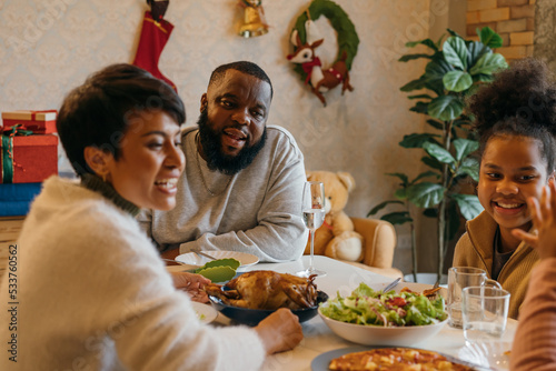 Happy young African American family of father  mother and two daughters enjoying christmas lunch of turkey and pizza at decorated house celebrating xmas and new years eve