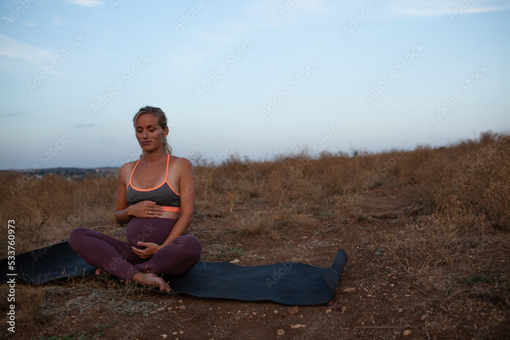 Pregnant woman makes yoga exercise outdoor in the meadow dry grass