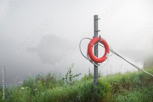 An orange life saving ring hangs on a metal post next to a fog covered pond in Stouffville, Ontario, Canada. photo