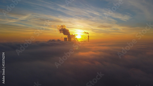 Top view of the clouds. Among the clouds there is a thermal power plant from which smoke is coming. The sun is shining behind
