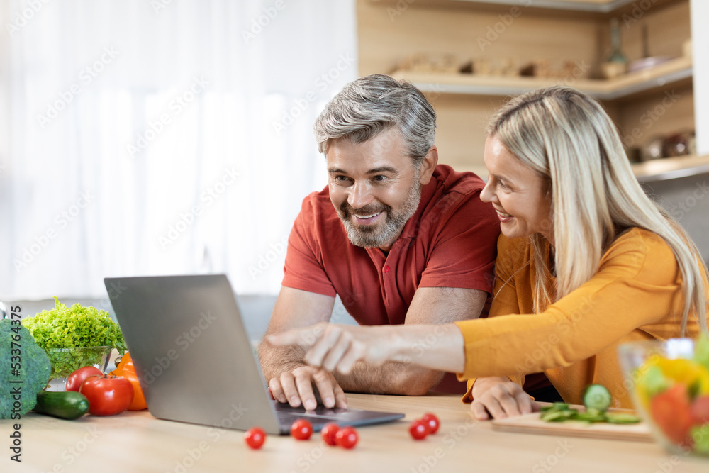 Happy middle aged spouses cooking together, reading food blog Happy middle aged spouses cooking together, reading food blog