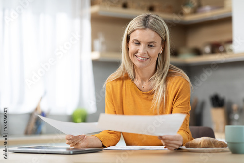 Cheerful blonde woman entrepreneur working from home, reading papers