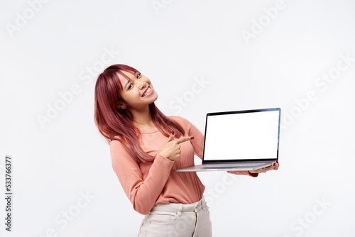 Young Asian smiling happy fun woman with showing a laptop over white background and pointing finger to screen with copy space for presenting website or product. Dressed in casual clothing. Isolated  photo