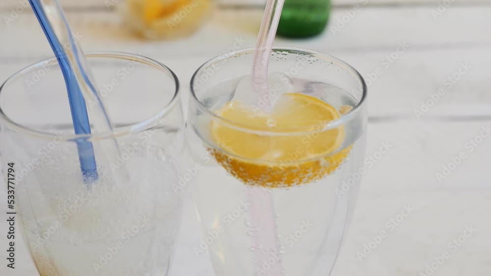 pour a refreshing carbonated drink into two glass glasses with pieces of ice and lemon slices. Glass reusable drinking straws are inserted into the glasses. lemon flavored soda. dolly shot pour a refreshing carbonated drink into two glass glasses with pieces of ice and lemon slices. Glass reusable drinking straws are inserted into the glasses. lemon flavored soda. dolly shot