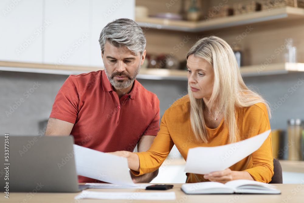 Obraz premium Middle aged husband and wife checking documents, kitchen interior