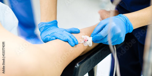 Installing a butterfly catheter in a patient's arm in a hospital. The introduction of a medicinal solution intravenously. Doctor's hands in sterile gloves insert a needle into a person's arm.