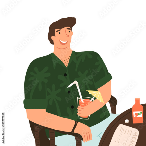 The young happy guy in the Hawaiian shirt sitting in the cafe and enjoying an orange soda lemonade, a cocktail. 