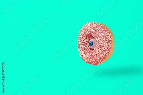 Human eye with Donut composition against a turquoise background. Halloween Santa Muerte and food concept.
