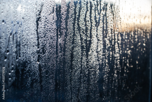 Texture of misted glass in winter. Frozen drops of water in sun on window. Dawn outside window. Abstract background. Selective focus.