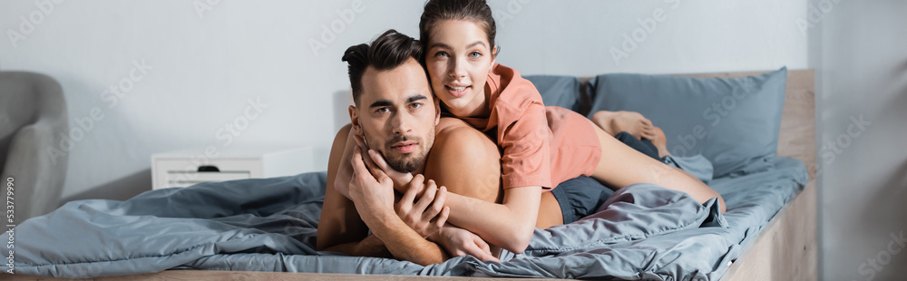 young couple of lovers embracing on bed and looking at camera, banner.