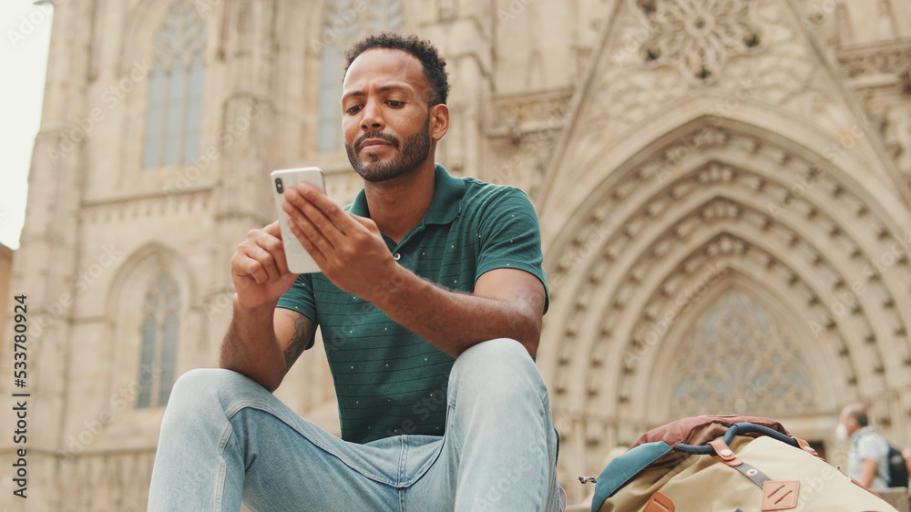 Close up, young man uses cellphone while sitting on the steps of the Sagrada Familia in Barcelona