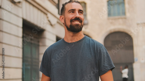 Young smiling man with beard walking and looking around at the old city background