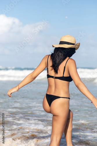 Wallpaper Mural Beautiful and sexy Caucasian woman in a black bikini and a wicker hat walking along the seashore on a summer day. Torontodigital.ca