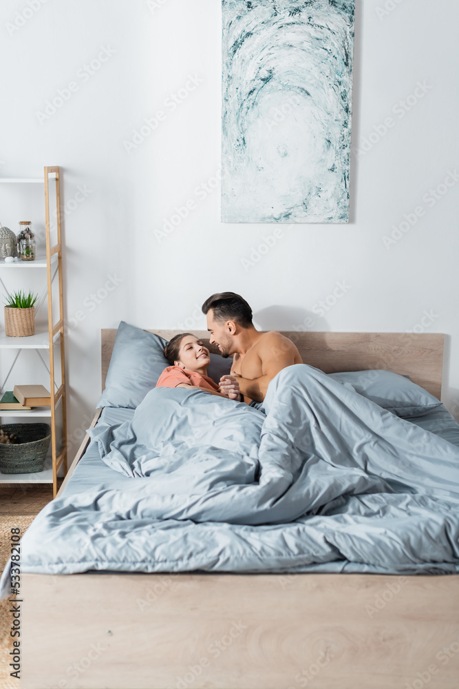 Fototapeta premium young sexy couple holding hands and smiling at each other while lying under grey blanket.