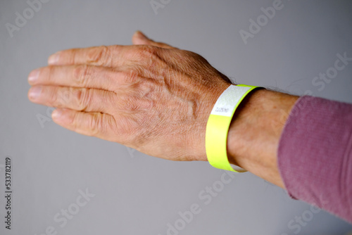 close-up of neon yellow paper bracelet on the male arm of adult clinic patient, check tape with entry number on hand of middle-aged european man, event ticket concept