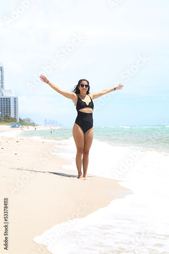 Caucasian woman, beautiful and sexy, black-haired, in a black bathing suit, laughing and dancing on the shores of the sea. Vacation and fun.