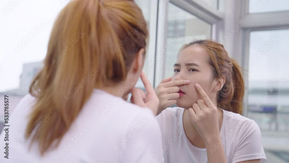 Asian woman is sad and worried because her skin is pimples and acne scars while looking in the mirror. Asian woman is sad and worried because her skin is pimples and acne scars while looking in the mirror.