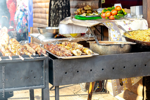 Close up detail view of chef tasty marinated pork meat and vegetables grilled at steel iron fire pit hearth table surface brazier with burning firewoods. Barbecue bbq yard home,street festival food photo