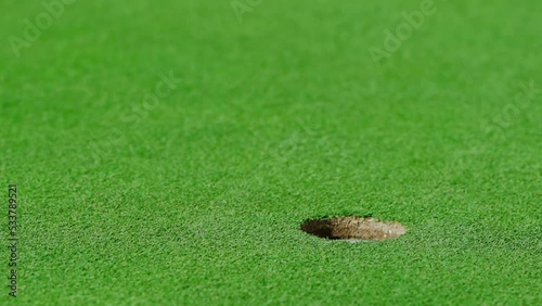 A golf ball after being hit by a club flies across the lawn into the hole