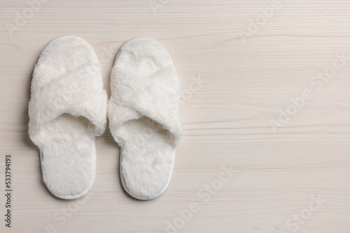 Pair of soft slippers on white wooden floor, top view. Space for text