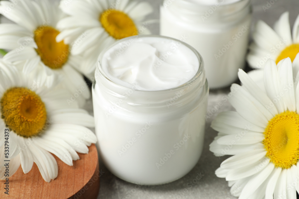 Jars of face cream and beautiful chamomiles on grey table Jars of face cream and beautiful chamomiles on grey table