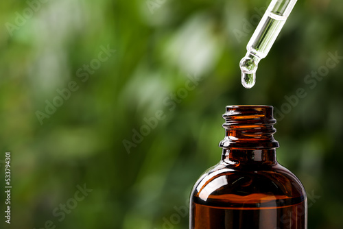 Dripping medical product from pipette into glass bottle against blurred background, closeup. Space for text