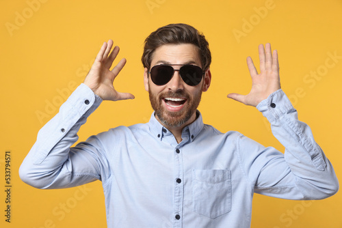 Portrait of excited bearded man with stylish sunglasses on orange background