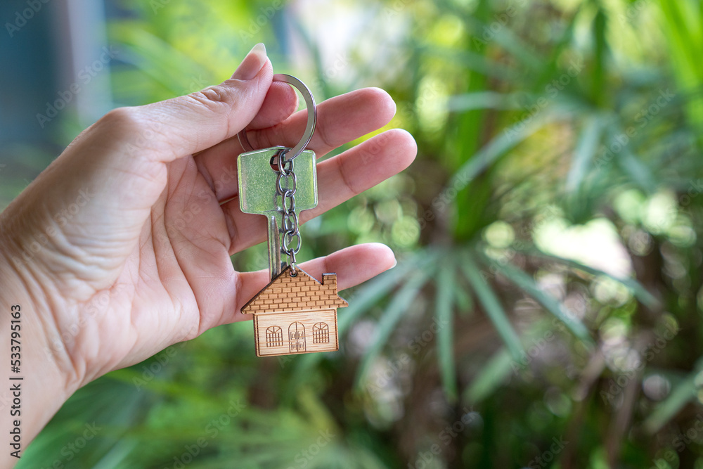 Fototapeta premium Hand holding house key with palm tree nature background. Home ownership concept.