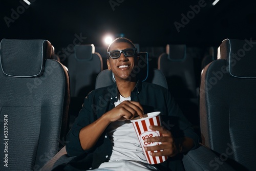 Φωτογραφία african american man in 3d glasses eating popcorn and watching film in cinema
