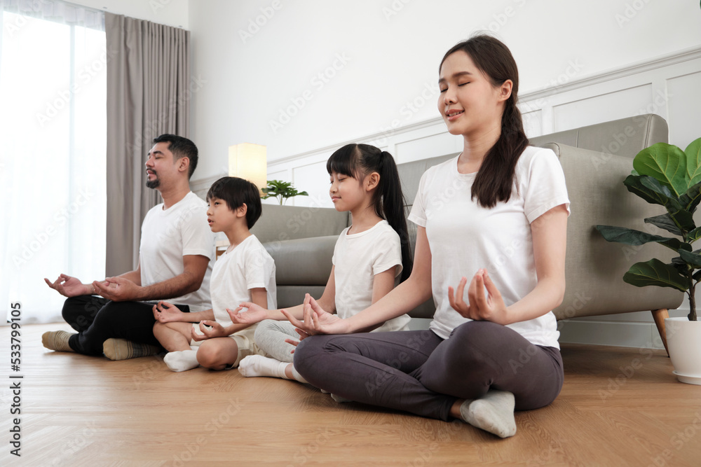 Happy Asian Thai family, parents, and children sit on living room floor, close their eyes together, tranquil meditate in lotus position, and practice healthy yoga, domestic home lifestyle weekend. Happy Asian Thai family, parents, and children sit on living room floor, close their eyes together, tranquil meditate in lotus position, and practice healthy yoga, domestic home lifestyle weekend.