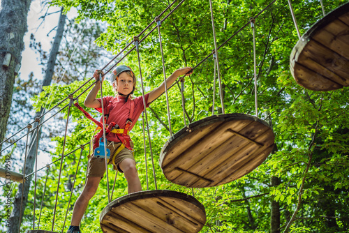 Obraz na płótnie Happy child in a helmet, healthy teenager school boy enjoying activity in a climbing adventure park on a summer day w salonie