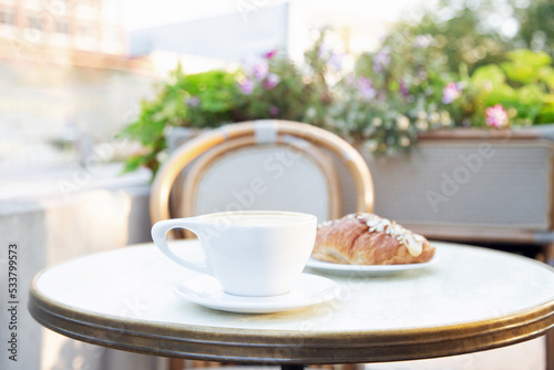 Cup of coffee and croissant on a patio table. 
Close up, blurred background.