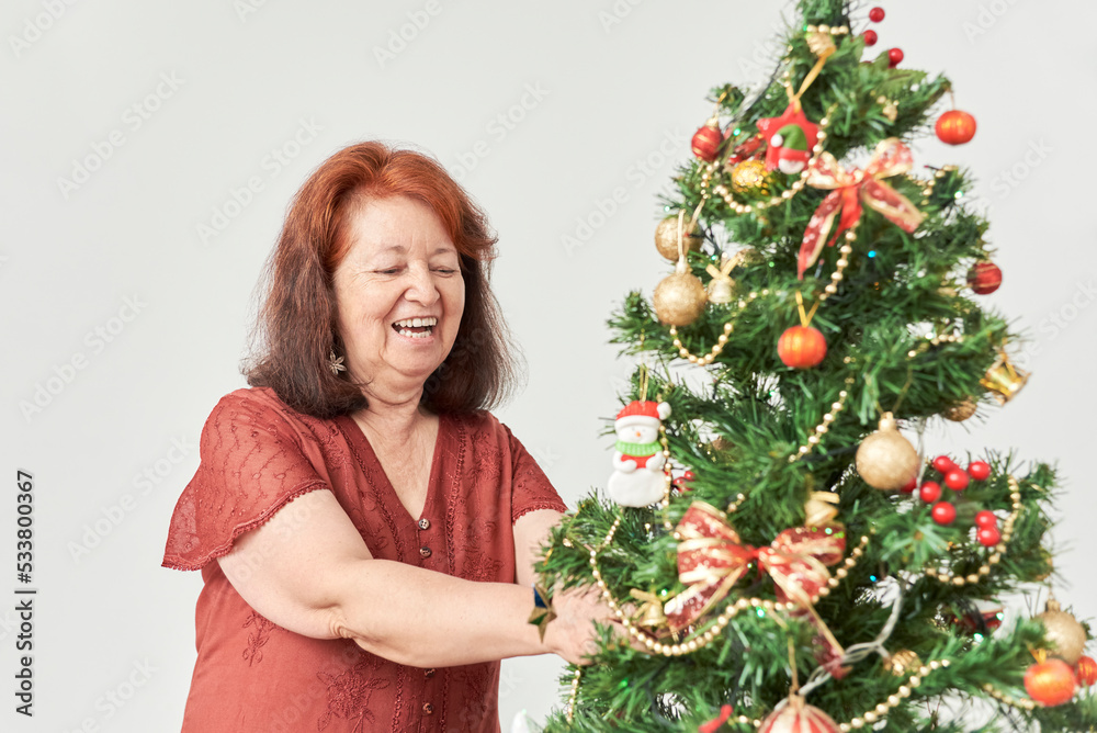 Happy mature hispanic woman smiling while decorating a Christmas tree at home. The joy of the holidays. Happy mature hispanic woman smiling while decorating a Christmas tree at home. The joy of the holidays.
