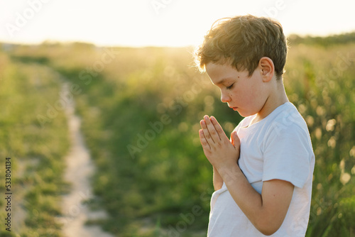 Foto Boy closed her eyes and praying in a field at sunset