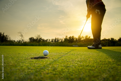 golfer putting a golf ball into a last hole on the green, golf course on summer sunset evening time with copy space