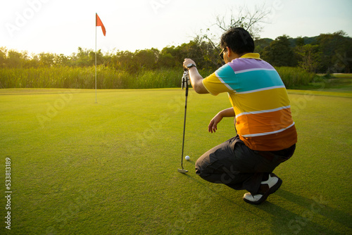 golfer putting a golf ball into a last hole on the green, golf course on summer sunset evening time with copy space